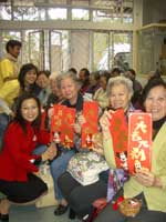 Hong Kong Disneyland Ambassador Angela To (far left, kneeling) distributes colorful Hong Kong Disneyland fai chuns to residents at the Fook On Church Social Centre for Elderly and celebrated the start of the Year of the Dog with them.